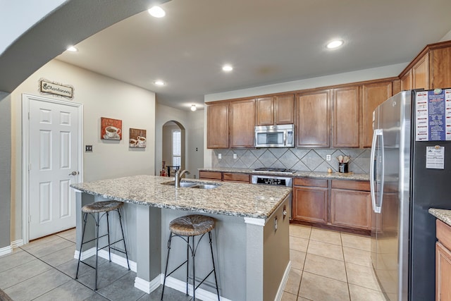 kitchen with arched walkways, a breakfast bar area, a kitchen island with sink, a sink, and appliances with stainless steel finishes