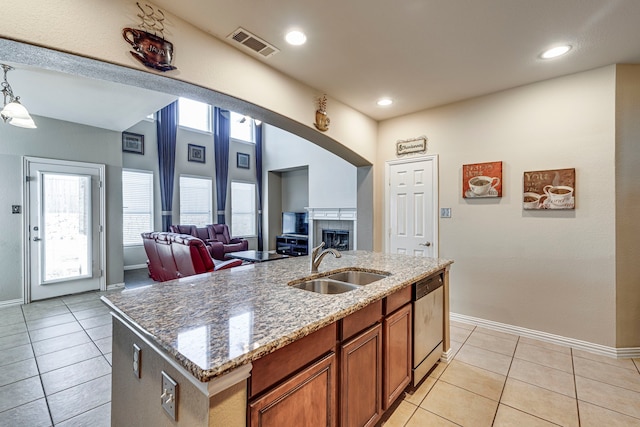 kitchen featuring light tile patterned floors, brown cabinetry, dishwasher, open floor plan, and a kitchen island with sink