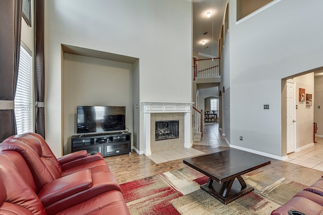 living room with a tile fireplace, light wood-style flooring, a high ceiling, baseboards, and stairs