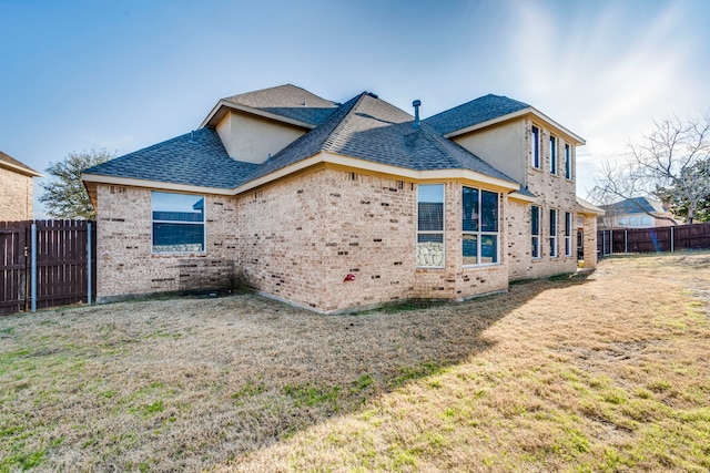 back of property with brick siding, fence, a lawn, and roof with shingles