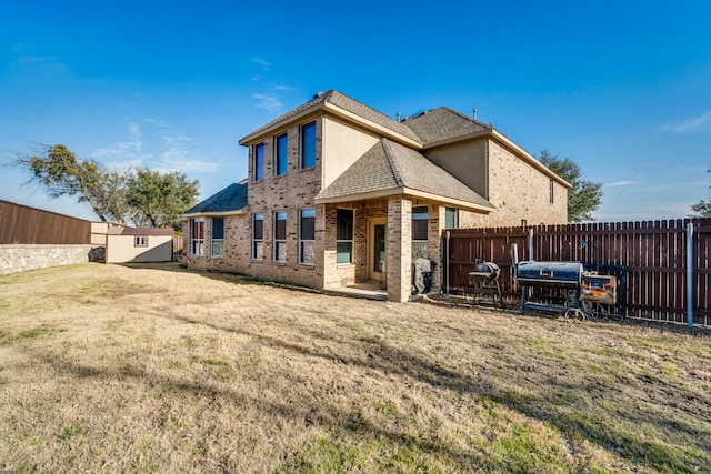 back of property with brick siding, a lawn, a shingled roof, and a fenced backyard