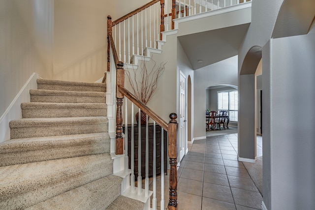 stairway with arched walkways, a high ceiling, tile patterned flooring, and baseboards