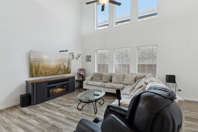 living room featuring a healthy amount of sunlight, a towering ceiling, light hardwood / wood-style flooring, and ceiling fan