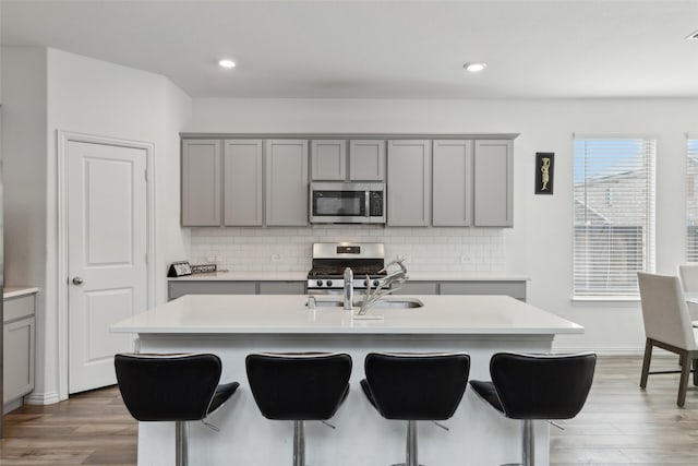 kitchen featuring stainless steel appliances, a kitchen island with sink, decorative backsplash, and gray cabinetry