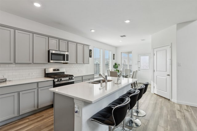 kitchen featuring a kitchen island with sink, sink, gray cabinetry, and appliances with stainless steel finishes