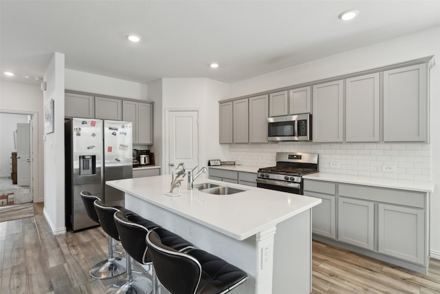 kitchen with sink, a breakfast bar area, backsplash, stainless steel appliances, and a center island with sink