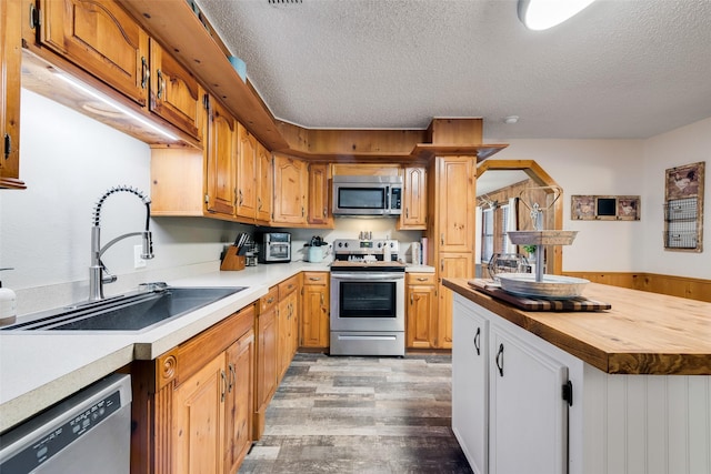 kitchen featuring appliances with stainless steel finishes, butcher block countertops, sink, light wood-type flooring, and a textured ceiling