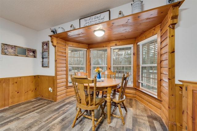 dining area with hardwood / wood-style flooring, a textured ceiling, and wood walls