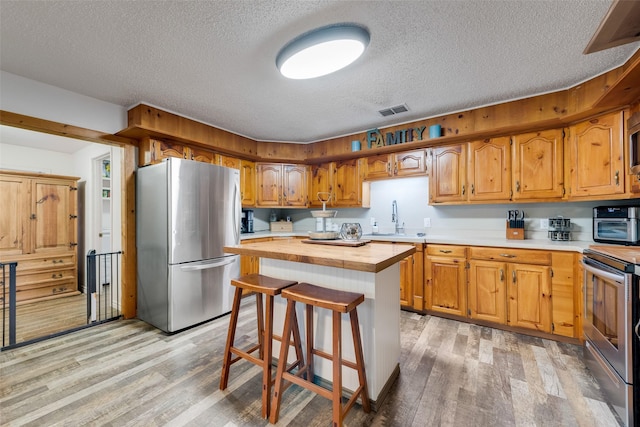 kitchen featuring appliances with stainless steel finishes, butcher block counters, sink, a center island, and light hardwood / wood-style flooring