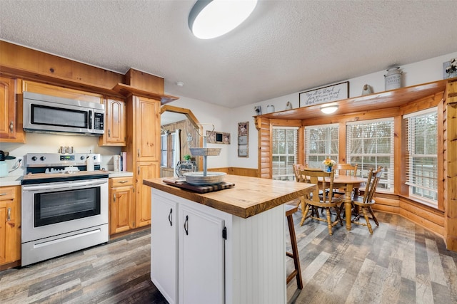 kitchen with wood counters, wood-type flooring, a center island, a textured ceiling, and appliances with stainless steel finishes