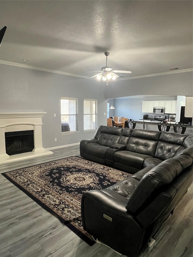 living room with ceiling fan, hardwood / wood-style flooring, ornamental molding, and a textured ceiling