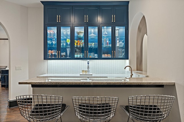 bar with dark wood-style floors, tasteful backsplash, and arched walkways