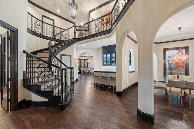 foyer entrance with a high ceiling, ornamental molding, dark wood-type flooring, and an inviting chandelier