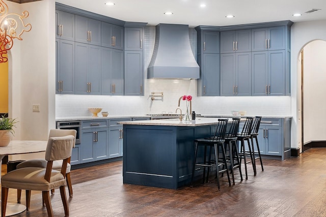 kitchen featuring a center island with sink, arched walkways, dark wood-style flooring, oven, and custom exhaust hood