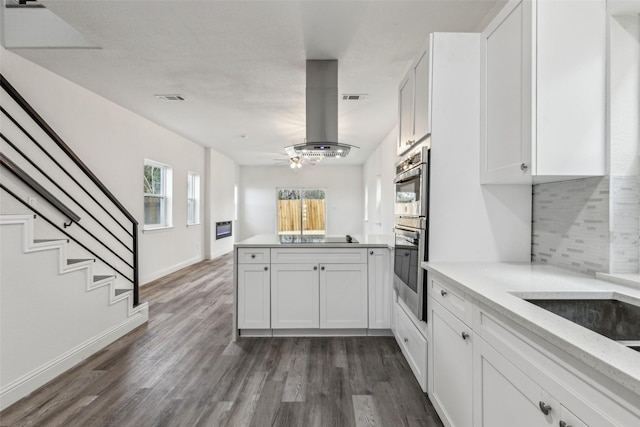 kitchen with dark hardwood / wood-style floors, tasteful backsplash, white cabinets, island exhaust hood, and stainless steel double oven