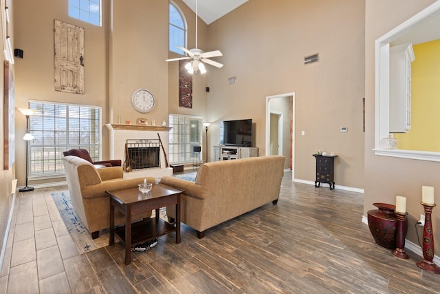 living room with a brick fireplace, a healthy amount of sunlight, dark wood-type flooring, and ceiling fan