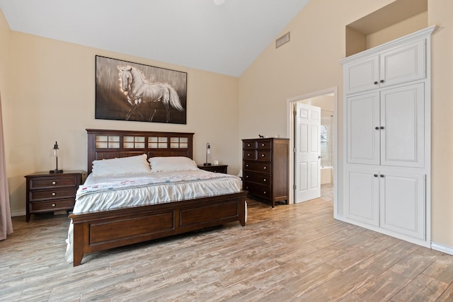 bedroom with ensuite bath, light hardwood / wood-style flooring, and high vaulted ceiling