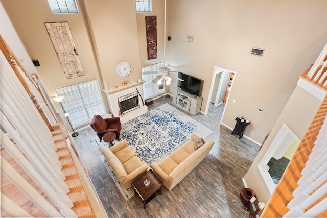 living room featuring a tiled fireplace, a high ceiling, dark wood-type flooring, and ceiling fan