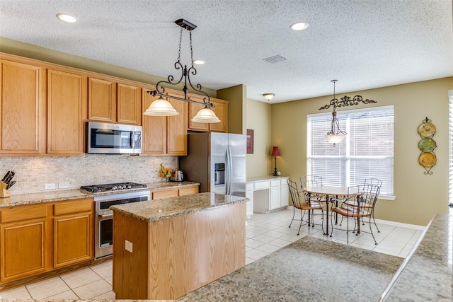 kitchen with pendant lighting, light tile patterned floors, stainless steel appliances, tasteful backsplash, and a kitchen island