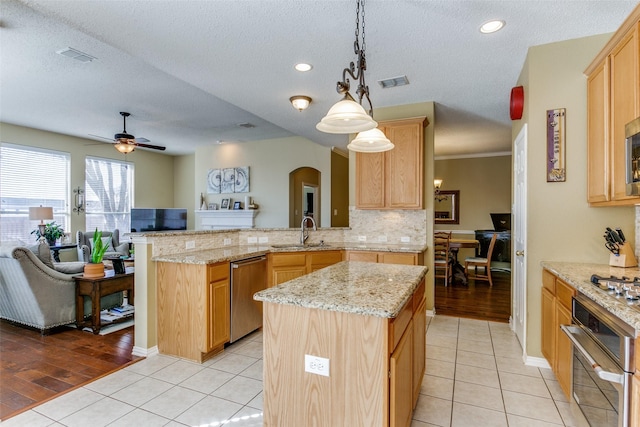 kitchen featuring stainless steel appliances, light brown cabinetry, kitchen peninsula, and a kitchen island