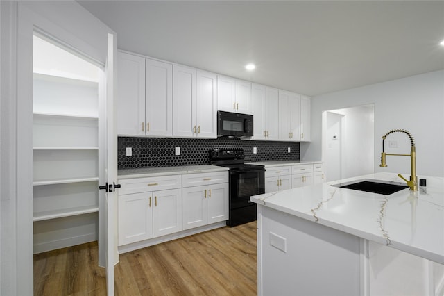 kitchen with sink, black appliances, light hardwood / wood-style flooring, light stone countertops, and white cabinets