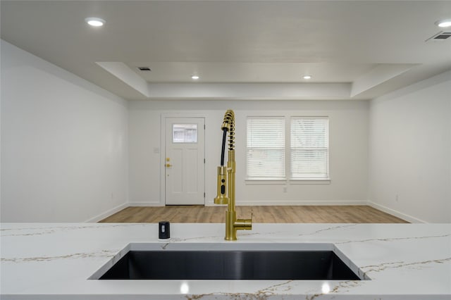 kitchen with light stone counters, a raised ceiling, sink, and light hardwood / wood-style flooring