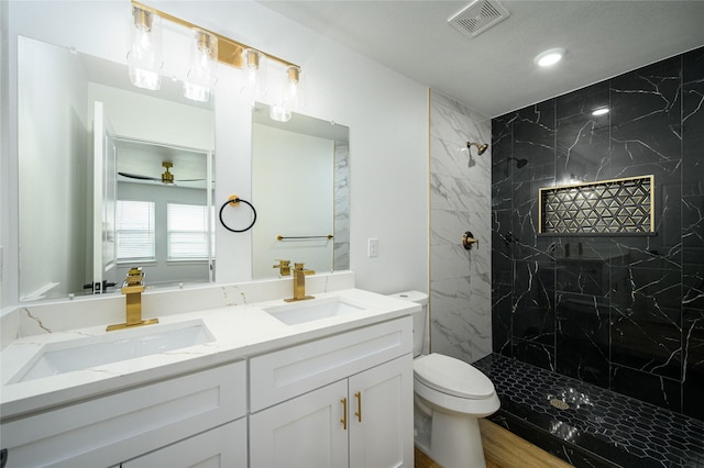 bathroom featuring vanity, a tile shower, ceiling fan, and toilet