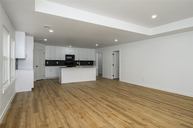 kitchen featuring sink, white cabinetry, an island with sink, light hardwood / wood-style floors, and decorative backsplash