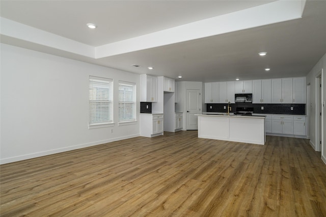 kitchen featuring range, white cabinetry, backsplash, a center island with sink, and light wood-type flooring