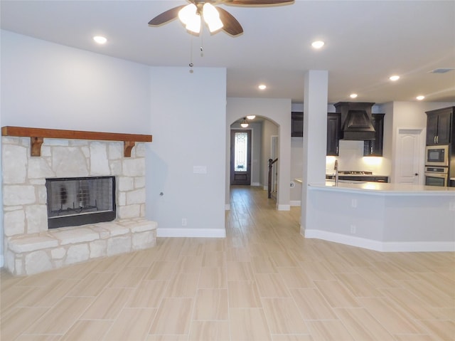 unfurnished living room with sink, a stone fireplace, and ceiling fan