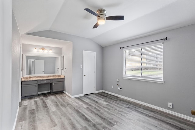 unfurnished bedroom featuring sink, ensuite bath, light hardwood / wood-style flooring, built in desk, and vaulted ceiling