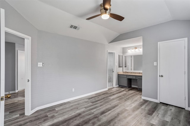 unfurnished bedroom with lofted ceiling, dark wood-type flooring, ceiling fan, connected bathroom, and built in desk