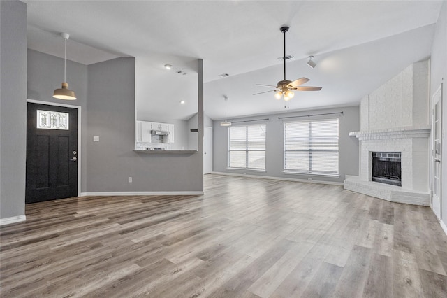 unfurnished living room featuring ceiling fan, high vaulted ceiling, a brick fireplace, and light wood-type flooring