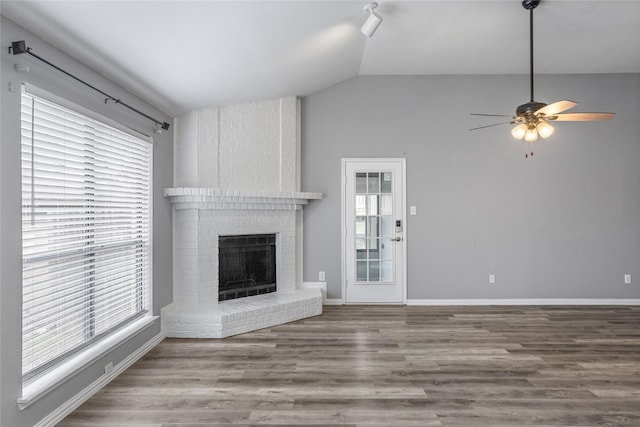 unfurnished living room featuring vaulted ceiling, a brick fireplace, wood-type flooring, and ceiling fan