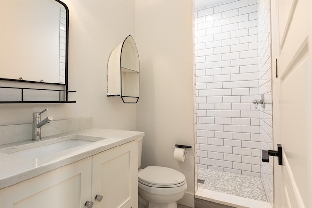 bathroom featuring vanity, a tile shower, and toilet