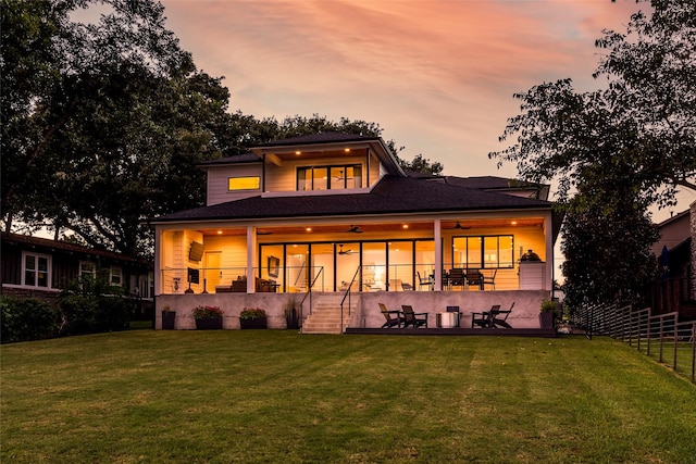 back house at dusk with a lawn, a balcony, ceiling fan, and a patio area