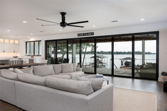 living room featuring sink, dark hardwood / wood-style floors, ceiling fan, and a water view