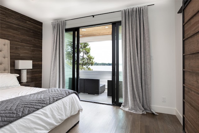 bedroom featuring a water view, wood-type flooring, access to outside, a barn door, and wood walls