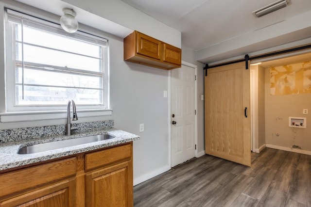 kitchen with light stone countertops, a barn door, sink, and dark hardwood / wood-style flooring