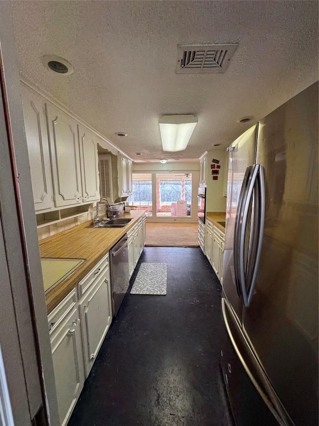 kitchen featuring concrete flooring, sink, a textured ceiling, appliances with stainless steel finishes, and white cabinets