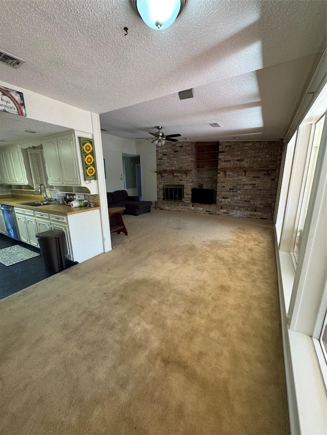 unfurnished living room with sink, light colored carpet, a textured ceiling, ceiling fan, and a fireplace