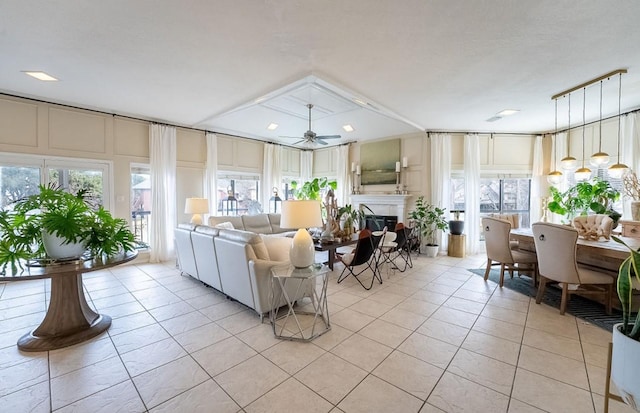 living area featuring light tile patterned floors, a glass covered fireplace, and a ceiling fan