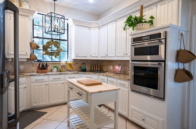 kitchen with double oven, tasteful backsplash, white cabinetry, and pendant lighting