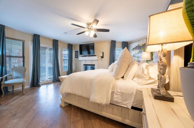 bedroom with baseboards, a ceiling fan, wood finished floors, and a glass covered fireplace