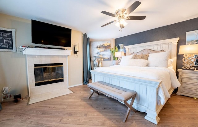 bedroom with light wood-type flooring, ceiling fan, and a fireplace