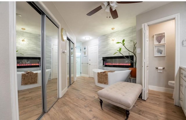 interior space featuring baseboards, ceiling fan, a glass covered fireplace, and light wood-style floors