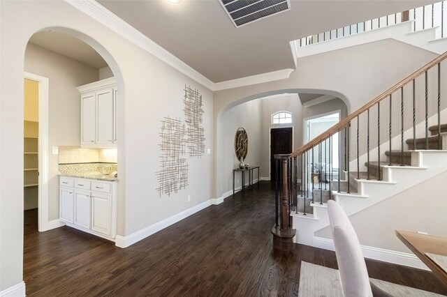 foyer entrance with ornamental molding, dark wood-type flooring, and a chandelier