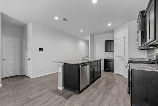 kitchen featuring sink, stainless steel appliances, light stone counters, light hardwood / wood-style floors, and a center island with sink