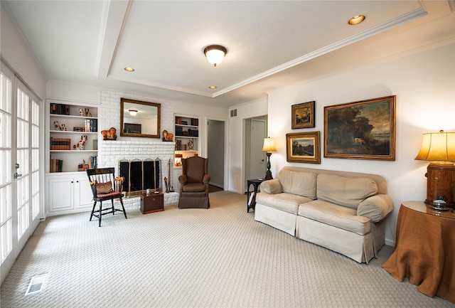 carpeted living room featuring built in features, ornamental molding, a raised ceiling, and a brick fireplace