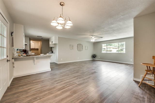 unfurnished living room featuring ceiling fan with notable chandelier, wood-type flooring, and a textured ceiling